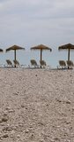 Portrait footage of the beautiful beach in Altea, Alicante in Spain showing sun loungers and straw beach umbrellas on the pebble beach known as Playa La Roda
