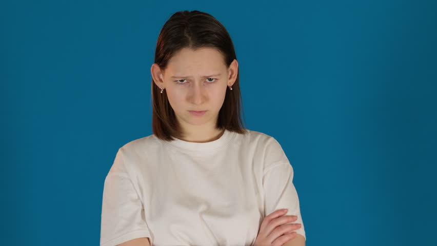 Lady body language conveys sense of defiance on blue background. Young woman jaw clenches with suppressed frustration during argue slow motion Royalty-Free Stock Footage #3485428487