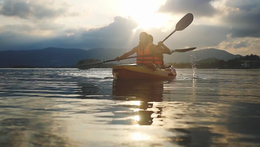 Happy smiling couple kayaking along the sea at beautiful summer sunset. Tourists paddling kayak, teamwork, togetherness. Slow motion. 1920x1080
