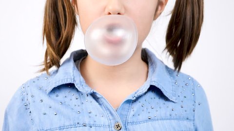 Slow motion close up portrait of cute girl chewing gum and blowing a bubblegum bubble ballon on gray wall