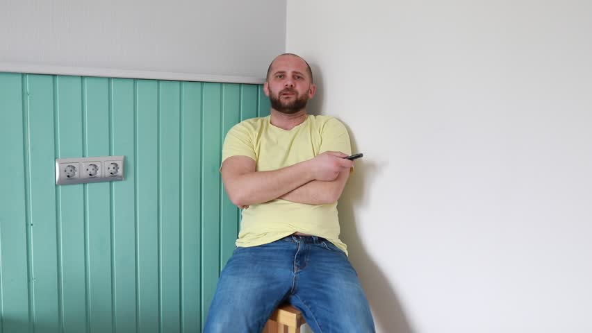 Man Sitting on Stool Against Mint Green Wall Holding Remote Control