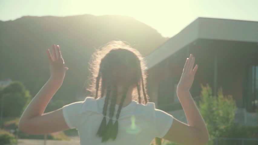Girl dancing in the summer sun, view from the back
