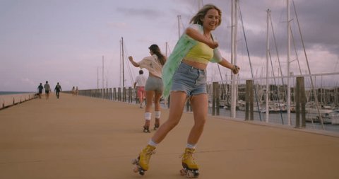 Inspiring shot of two best friends or queer women rollerblade and doing tricks together. Summer happy outdoor activity. Colorful outfits and joy of elusive moment. Freedom and female empowerment.の動画素材