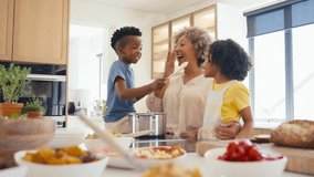 Grandchildren helping grandparents in kitchen preparing food for meal as grandson puts food on grandfather's nose - shot in slow motion - Powered by Shutterstock - Get 15% off with code: PIKWIZARD15