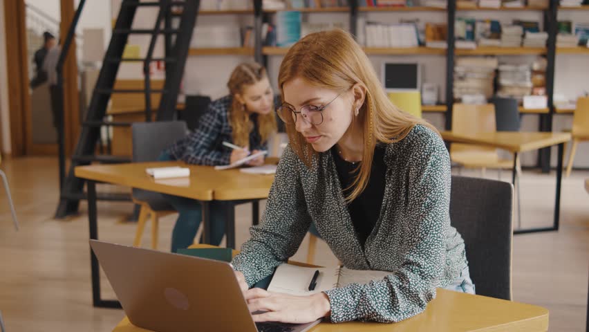 a group of students study and read books, write information in notebooks, on their phones and laptop in a library or classroom. Students in a good mood studying and reading books in the library