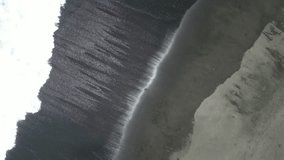 Drone video of the sparkling black sand beach from above in Bali. Top view of ocean, waves, and black volcanic sand