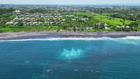 Aerial drone video of beautiful black sand beach, turquoise ocean, waves, coastline, rice terraces, tropical palm paradise in Bali. Indian Ocean from above.