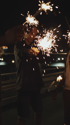 Vertical shot of young multi-ethnic men and women holding sparklers enjoying dancing at party on summer night