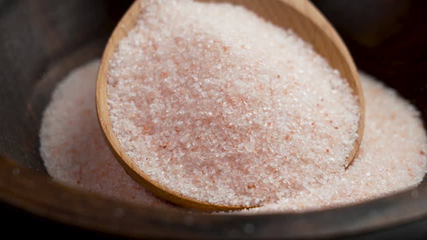 Pile of pink Himalayan salt in wooden spoon close up. Exotic cuisine ingredients. Rotation