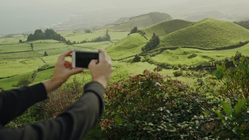 Young man hold smartphone and make video of beautiful green hills. Male take picture of scenic landscape with valley using mobile phone camera