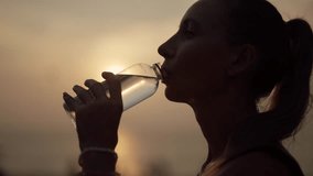 Woman drinking water after training. Fitness thirsty girl drinks water during workout pause, after a grueling run of a long sea ocean beach at sunset. Endurance fitness, morning run concept. - Powered by Shutterstock - Get 15% off with code: PIKWIZARD15