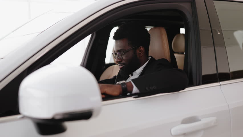 Calm African man, customer, buyer, client in suit holding hands on steering wheel choose auto want buy new automobile in car showroom vehicle salon dealership store motor show indoor. Sales concept. Royalty-Free Stock Footage #3486028205