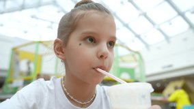 Little girl child drinking milkshake in food court, close-up. Cute girl drinking vanilla milkshake from cup with straw