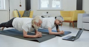 Active healthy senior man and woman simultaneously revision video lessons on laptop doing elbow plank on mats while training at home