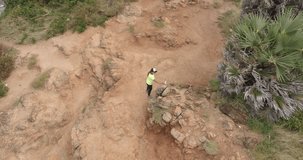 Video from drone. Sportive beautiful girl running by rocky road at cliff washed by sea on a sunny day. The woman run between rocks. Hiking. Outdoor taining. Nai Harn cliff, Phuket island, Thailan.