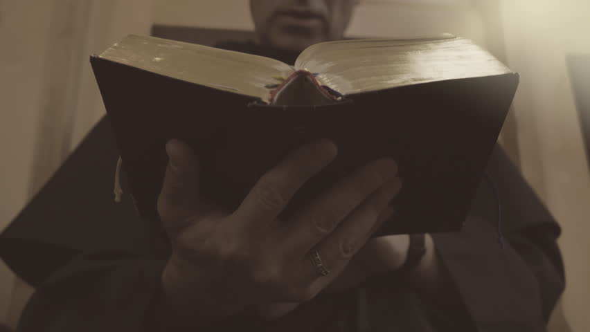 Christian monk in robe reading bible close up. Catholic church priest standing up with psalmbook in hands, low angle view