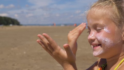 The girl apply sunscreen to face and body. The girl squeezes the sunscreen into her palm and puts it on her face.