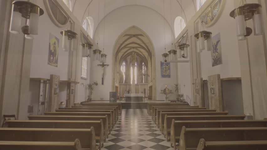 Moving backwards through aisle from altar in empty church. Christian cathedral interior with wooden pews rows, sanctuary and black and white tile floor wide shot