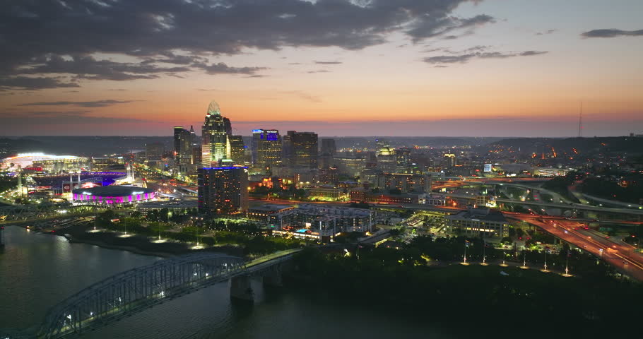 Driving cars on bridge highway near illuminated high skyscraper buildings in downtown district of Cincinnati, Ohio, USA. American city with business financial district at sunset.