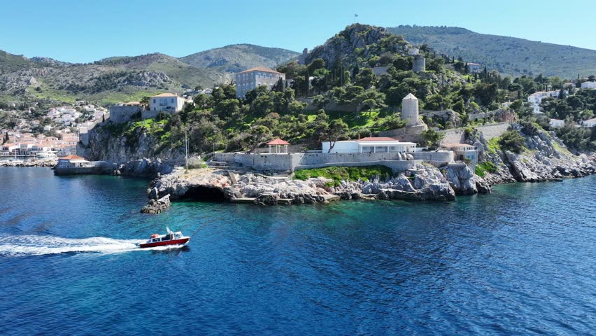 Aerial drone cinematic video of water taxi cruising near picturesque and historic main village of Hydra or Ydra island well know for captain's mansions and marine tradition, Saronic gulf, Greece