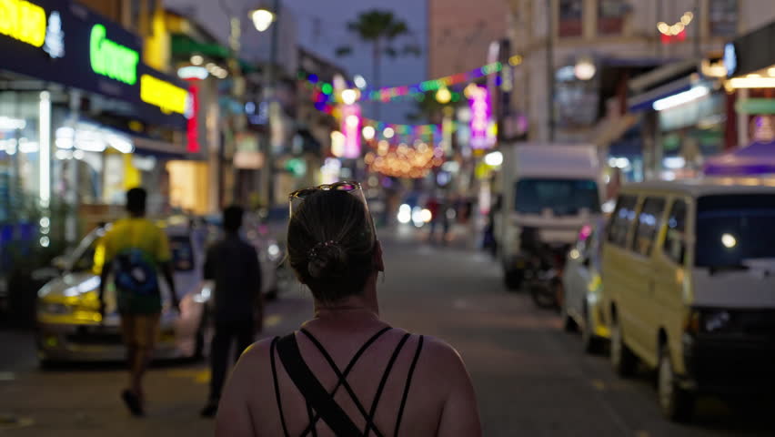 Rearview of female traveller walking alone while exploring city streets and enjoying the night scene in George Town, Penang, Malaysia, Southeast Asia
