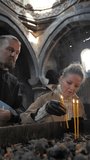Vertical video: a young woman placed a lit candle on the altar in a Christian church in the company of a young priest with a beard and a fashionable hairstyle. Christianity concept