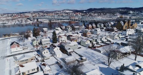 A slow forward winter aerial establishing shot of snow covered roads and houses in a rust belt residential neighborhood. Rochester and Ohio River in the distance. Pittsburgh suburbs.  	