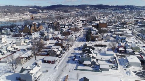 A slow forward winter aerial establishing shot of snow covered roads and homes in a rust belt residential neighborhood. Rochester and Ohio River in the distance. Pittsburgh suburbs.  	