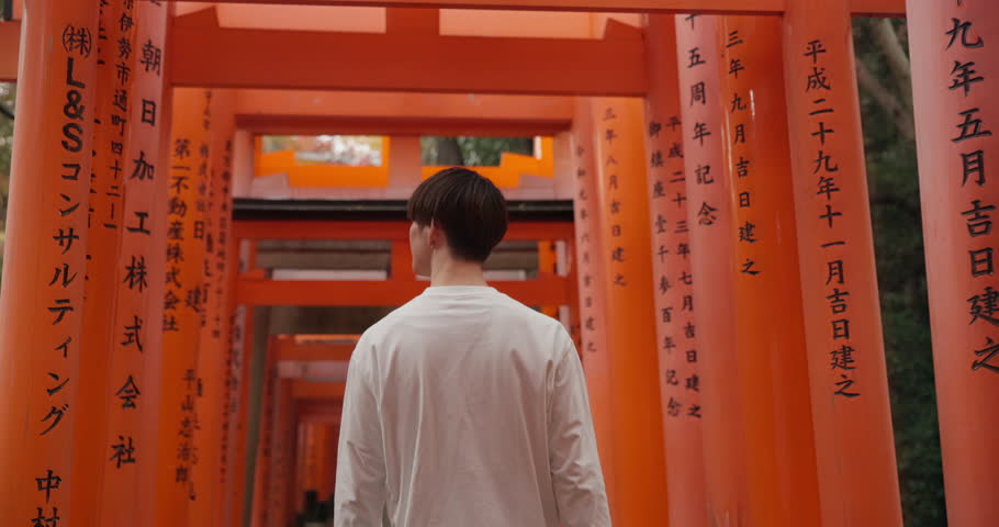 Travel, location and Japanese spiritual shrine in Kyoto with man walking on trail for religion, god and mountain. Fushimi Inari Taisha, monument and back of person experience Torii gates on adventure