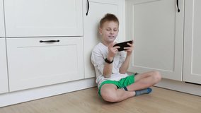Young Boy Playing Handheld Video Game on Kitchen Floor During Daytime