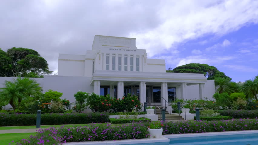 Establishing shot of Laie Hawaii Temple on a cloudy day. A view of white Mormon church amidst greenery and flowers. Hawaiian temple in overcast weather.