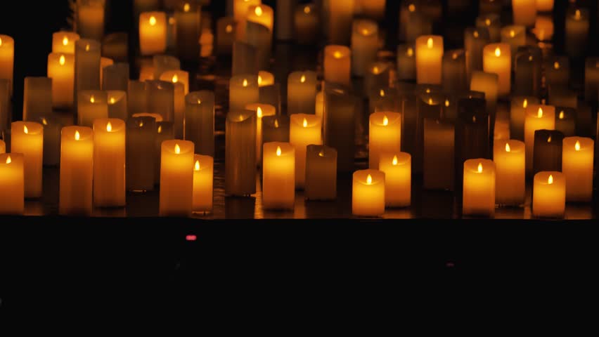 A multitude of electric candles burning in a darkened hall. A modern and safe alternative to traditional candles. The soft, flickering light of the candles creates a serene and peaceful atmosphere Royalty-Free Stock Footage #3486598551
