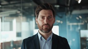 Close up of positive caucasian male smiling widely while standing against translucent expanse of office wall. Attractive businessman wearing dark formal suit showing resolve in the workplace. - Powered by Shutterstock - Get 15% off with code: PIKWIZARD15