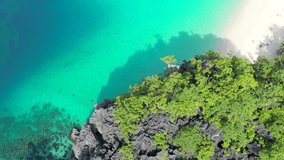 The sun casts a warm glow on the edge of a verdant cliff overlooking a turquoise sea, with a single kayak as a silent witness. Video capturing the beauty of a tropical. Aerial shot with slow motion. 