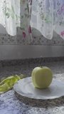 Vertical video with a woman's hand cutting a piece of juicy green apple on a white plate with natural sunlight coming through the kitchen window.