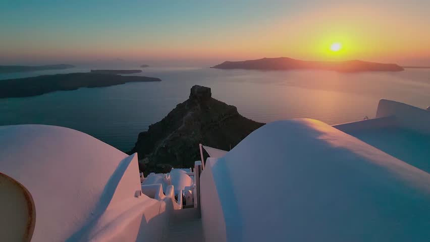 Romantic sunset over the rooftops of Santorini. White facades of houses. View of the sea horizon. Greece