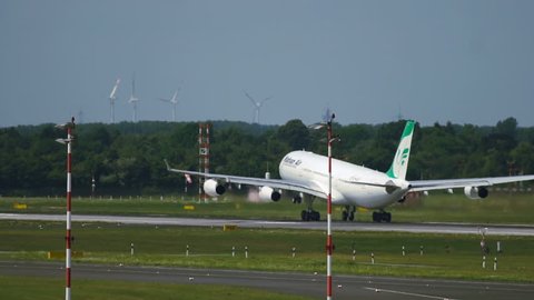 DUSSELDORF, GERMANY - JULY 23, 2017: Rear view of Airbus A340 of Mahan Airlines accelerates on runway and takes off at Dusseldorf International Airport. Windmill at the background. Slow motion