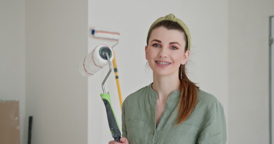 Do-it-yourself interior decorating. Joy and satisfaction in her self-directed home renovation project. A young woman is captured smiling as she embarks on painting the walls of her new apartment Royalty-Free Stock Footage #3486750005