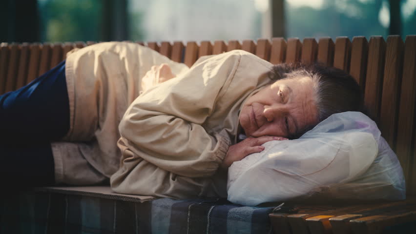 Poor senior woman waking up on bench in park, homelessness and poverty problem