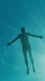 A man swims on the surface and then dives into the depths of the sea. Underwater view. Vertical Video