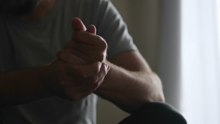 In a shadowy room, a man's hands tell a story of mental anguish through constant fidgeting and nervous gestures.