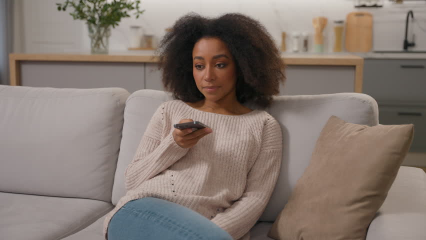 African American woman ethnic girl on couch talk smartphone using speakerphone convenient usage cell phone female lady homeowner recording voice mail with mobile app answering on audio message at home Royalty-Free Stock Footage #3486840555
