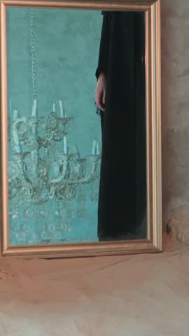 Young beautiful woman in black arabic national dress abaya walking barefoot around chandelier on mirror background