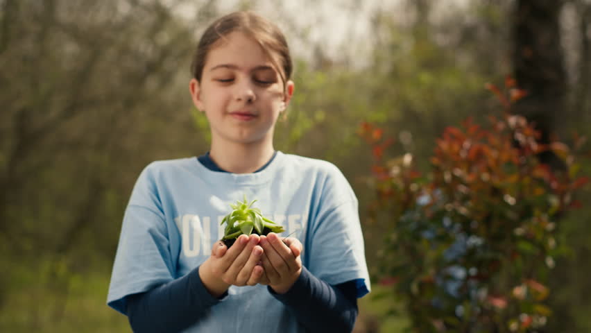 Little kid volunteer holding a small seedling with natural soil in hands, presenting plant for new habitat in the forest. Child fighting nature preservation, environmental care awareness. Camera A. Royalty-Free Stock Footage #3486915543