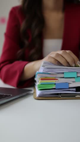 A woman doing paperwork is searching for a sheet of paper in a pile of documents on her desk.