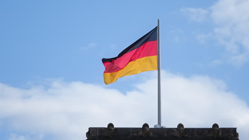 Germany flags wave against blue sky. Deutschland government symbol close up. City street background. Patriotism proud concept. National german silk flag on building roof top. Berlin sign fluttering.