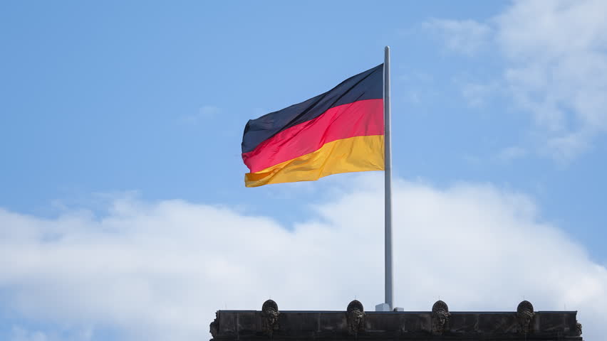 Germany flags wave against blue sky. Deutschland government symbol close up. City street background. Patriotism proud concept. National german silk flag on building roof top. Berlin sign fluttering.
