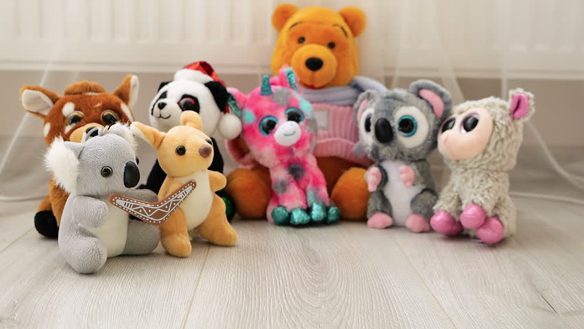 Stuffed and fluffy Pink Piglet plush toy falls on the laminate in the play area against the background of other toys. Slow motion.