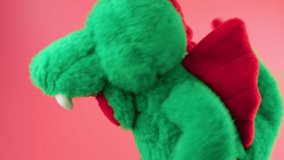 Stuffed and fluffy plush toy green dragon playing and dancing on a pink background.