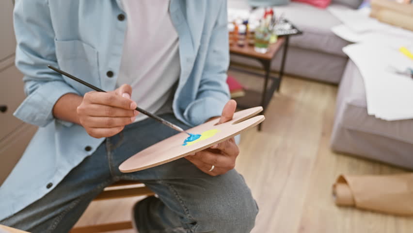 A cheerful man painting with a palette and brush in a cozy home studio setup